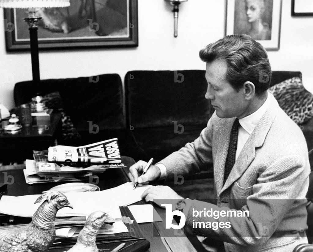 Jacques Sernas signs some documents, seated at a desk