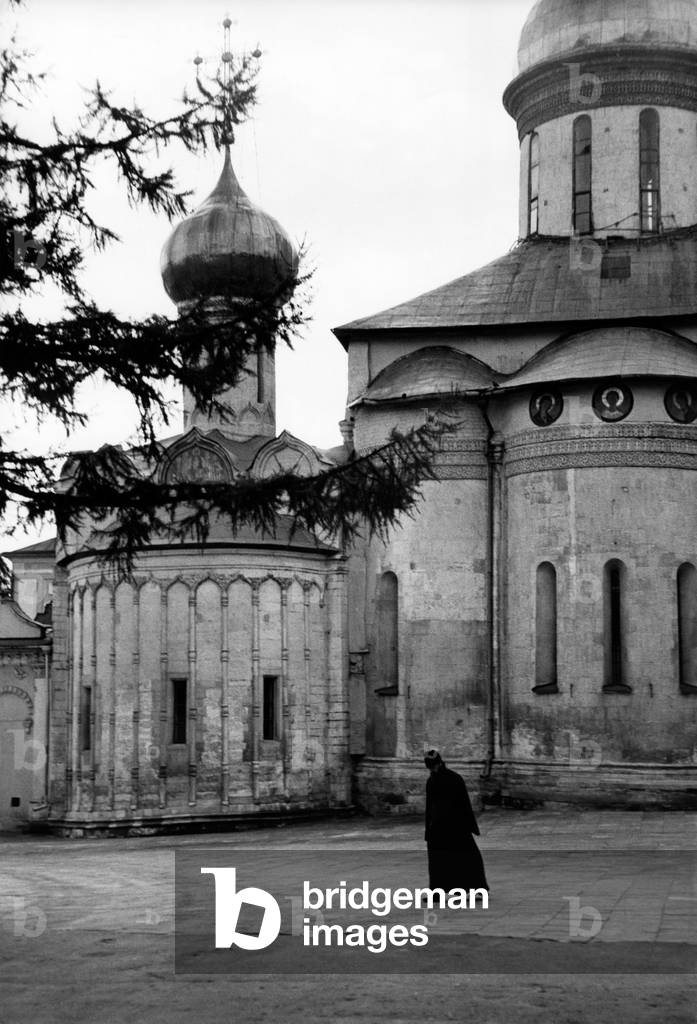 An Orthodox monk is walking outside the apse of the Cathedral of the Holy Trinity in the Monastery of Zagorsk