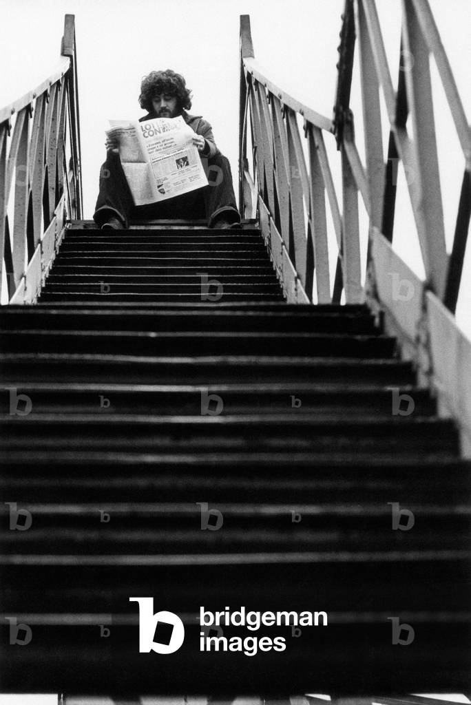 A young man reading the newspaper Lotta continua sitting on a staircase