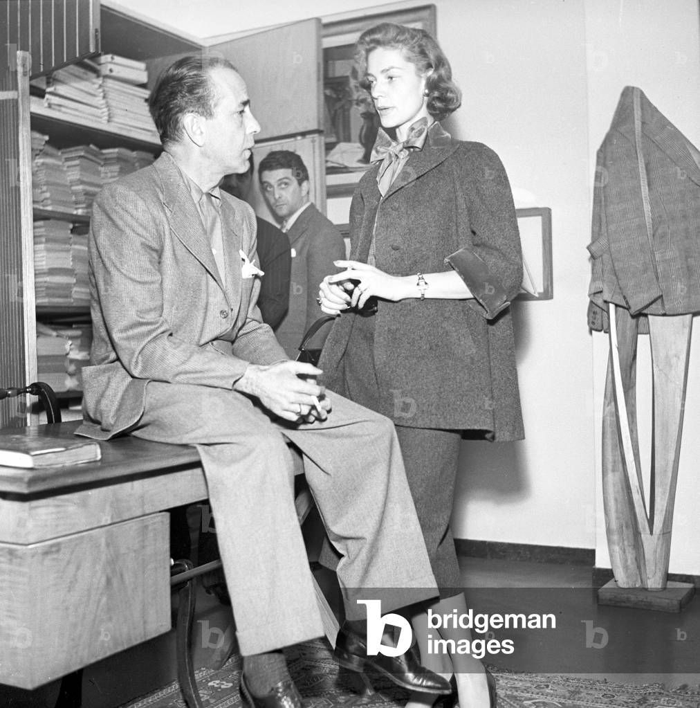 Humphrey Bogart and Lauren Bacall talking in the Battistoni tailor's shop, Rome, Italy, 1950 (b/w photo)