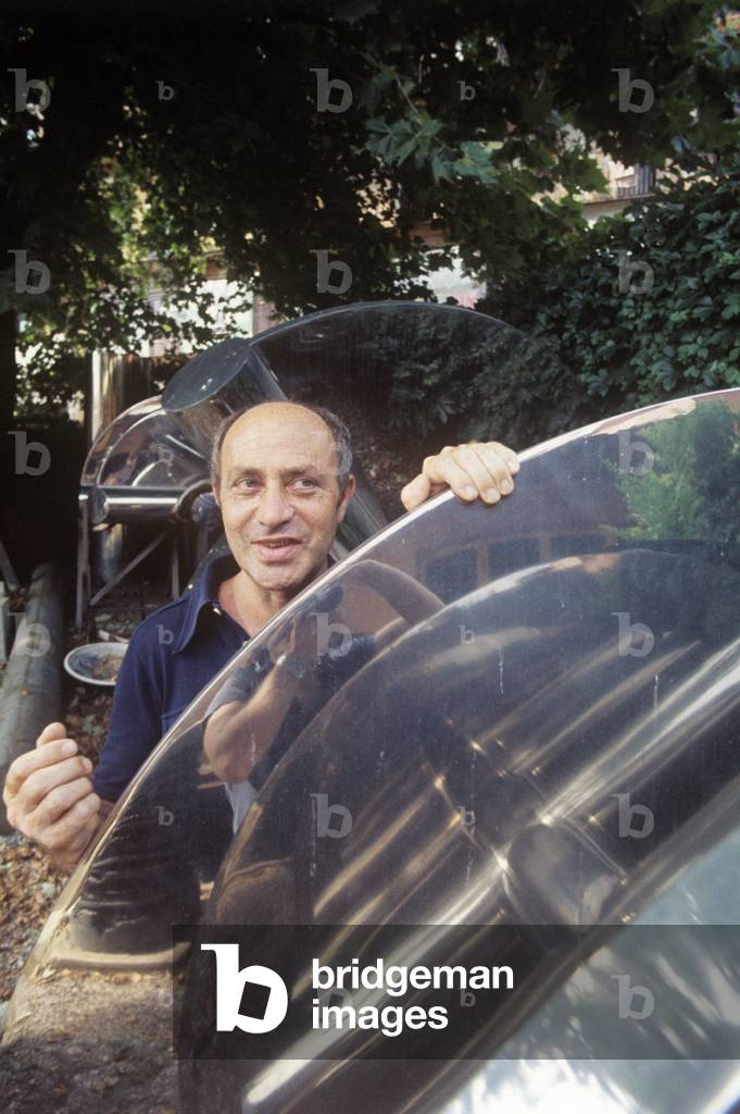 Arnaldo Pomodoro in the garden leant against one of his artworks