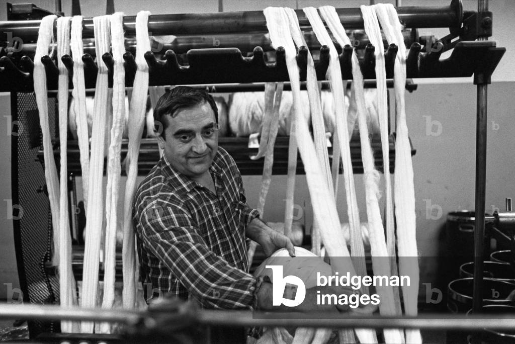 A workman gathering together the yarns of a woolen mill in the district of Biella, Italy, 1968 (b/w photo)