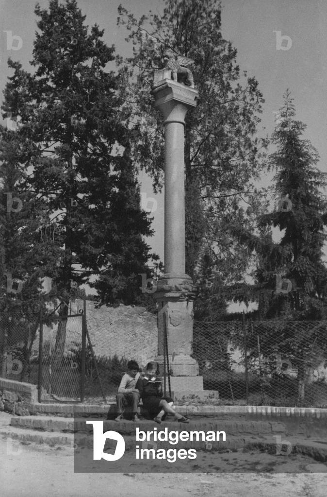A boy and a girl sitting under the column on Piazza San Marco in Arquà  Petrarca, Arquà  Petrarca, Italy