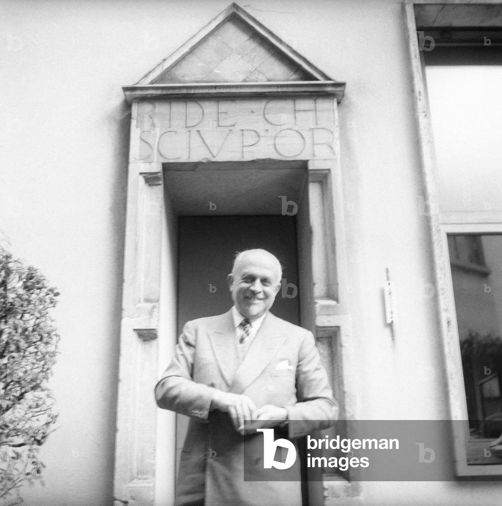 Piero Portaluppi smiling in front of a door with an inscription