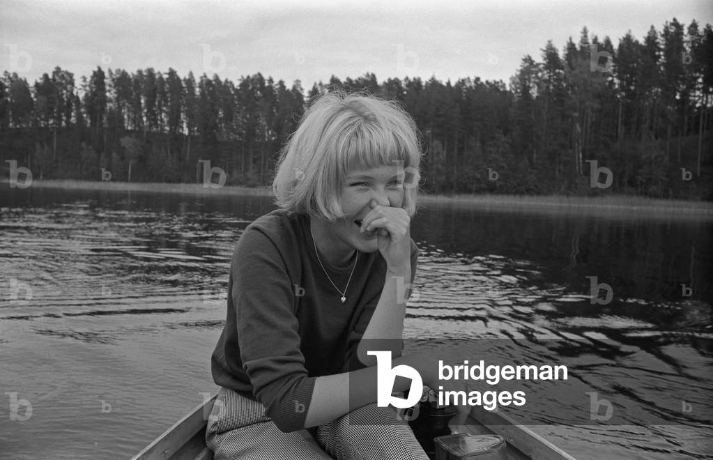 A young Finnish woman smiling seated on a rowing boat, Finland, 1960s (b/w photo)