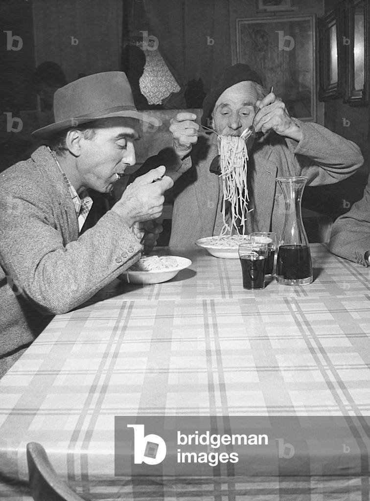 Two men eating spaghetti at the restaurant, Italy, 29th July 1955 (b/w photo)
