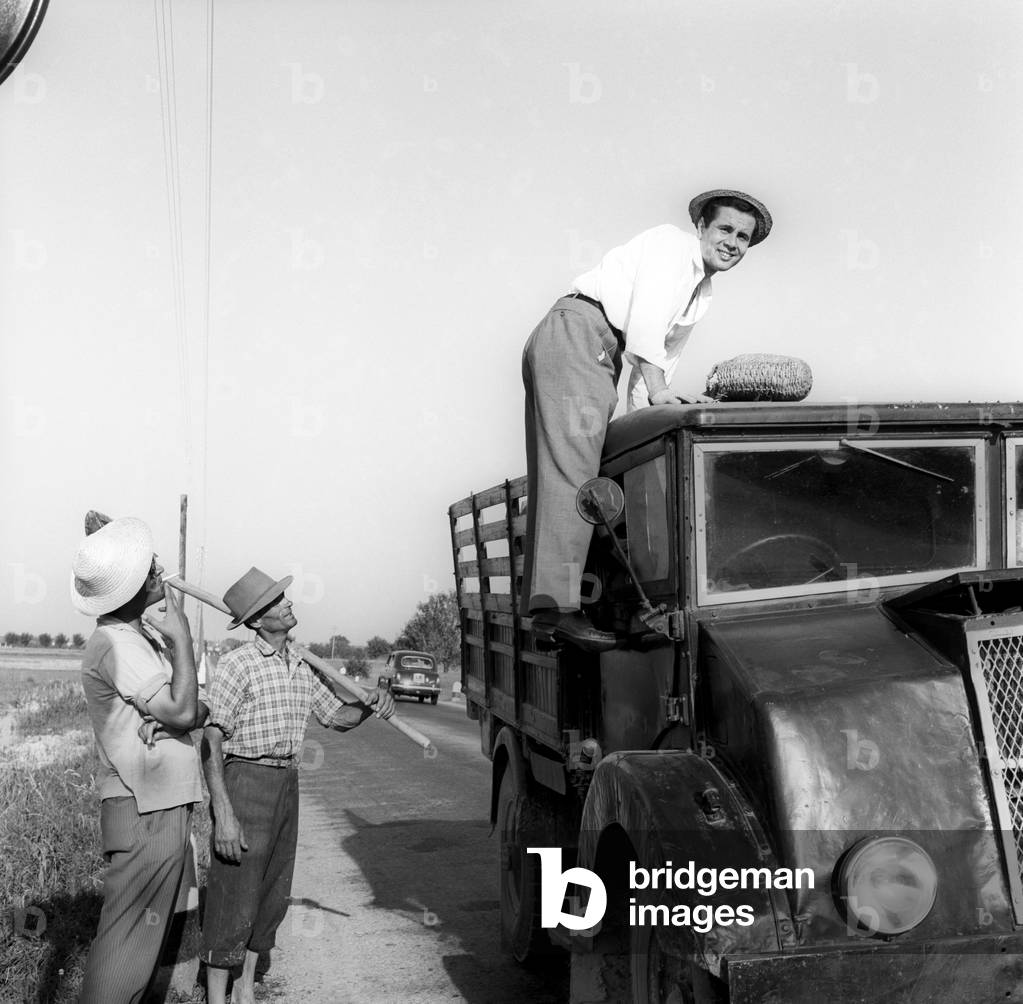 Enzo Tortora standing on a truck observed by two farmers