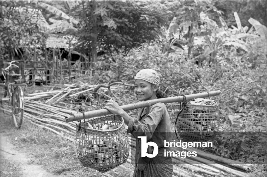 Thai little girl carrying trunks into two baskets, Bangkok, 1961 (b/w photo)