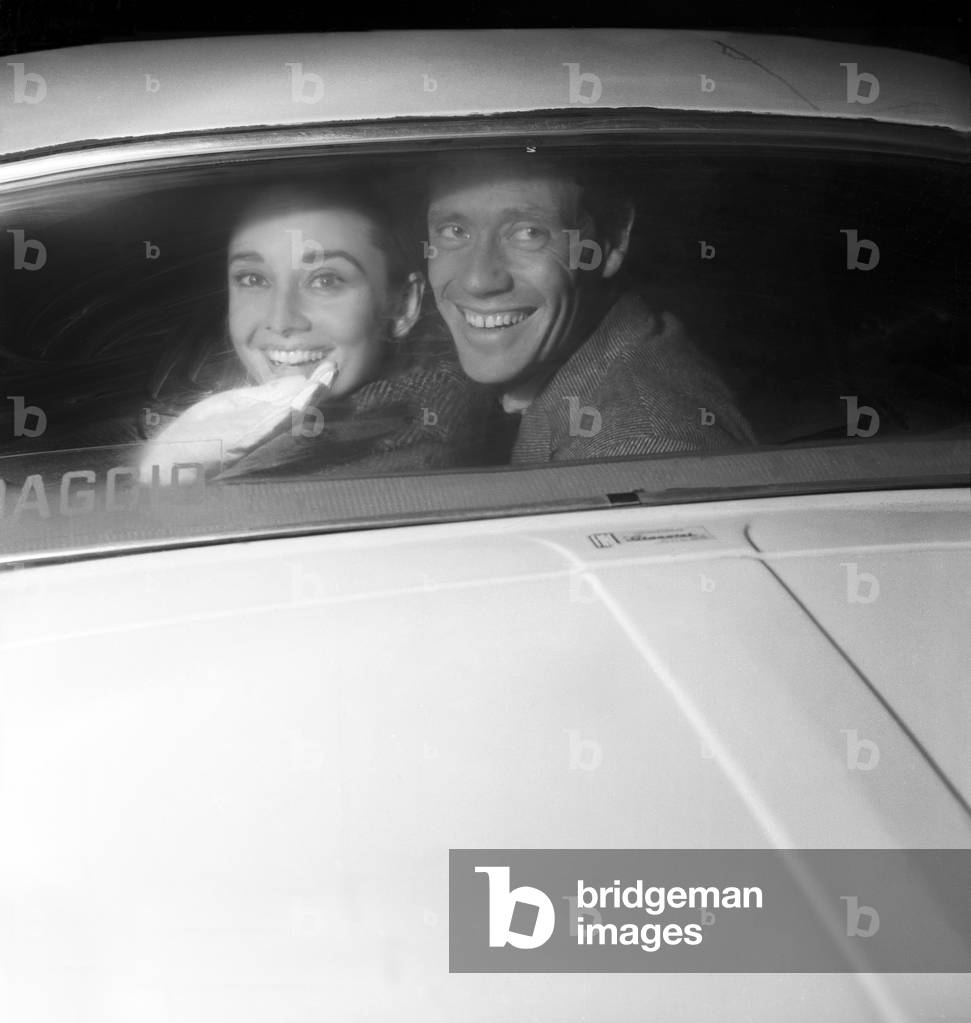 British actress Audrey Hepburn and American actor Mel Ferrer smiling inside a car, Ciampino, Rome, Italy, 1958 (b/w photo)