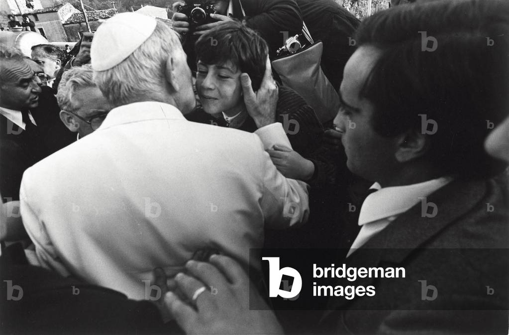 Pope John Paul II is kissing a young boy during a visit to the villages struck by the earthquake of 1980