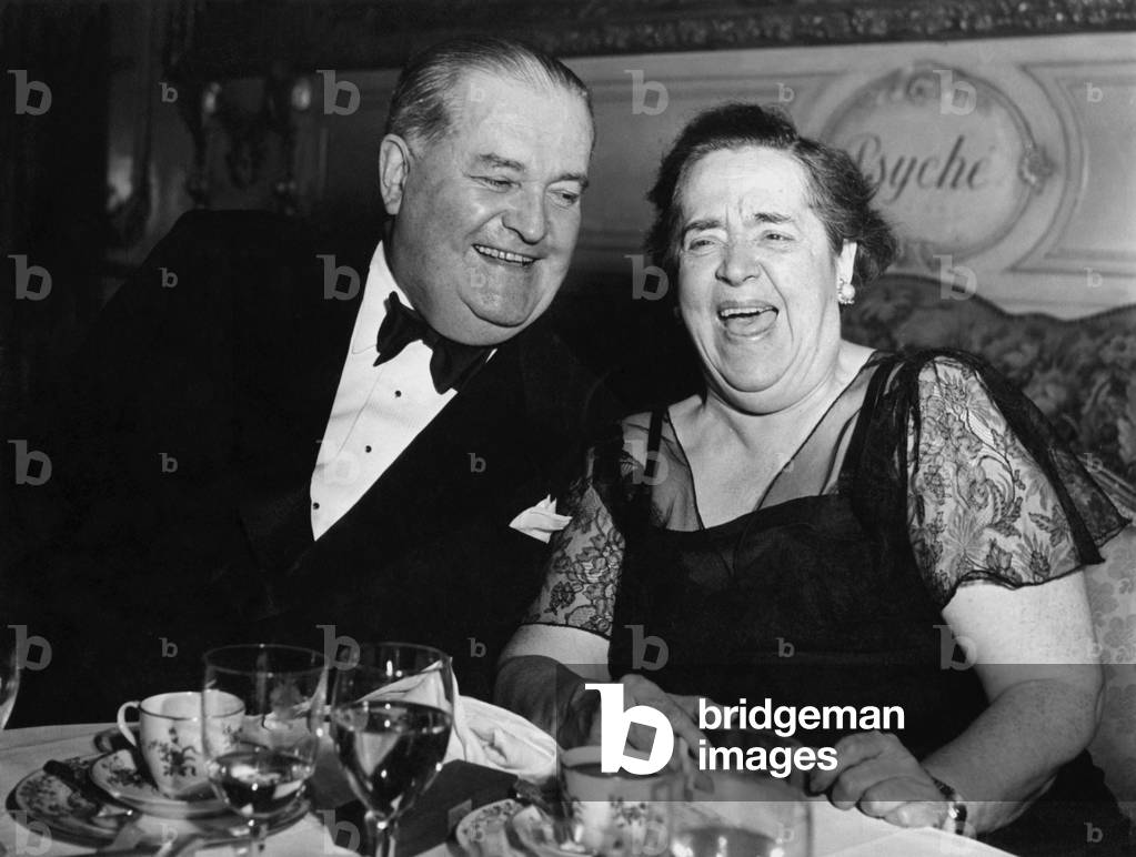 Elsa Maxwell sitting at the table and laughing, 1950 (b/w photo)