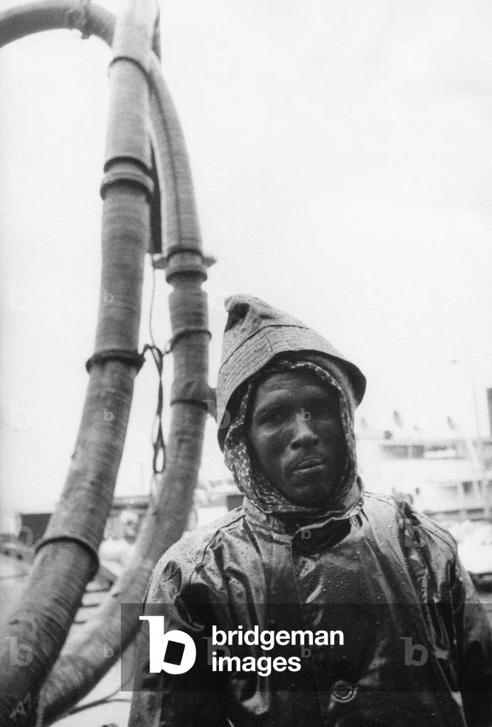 Half-length portrait of a worker wearing a raincoat, on the background of the pump of an oil field, Ahmadi, Kuwait