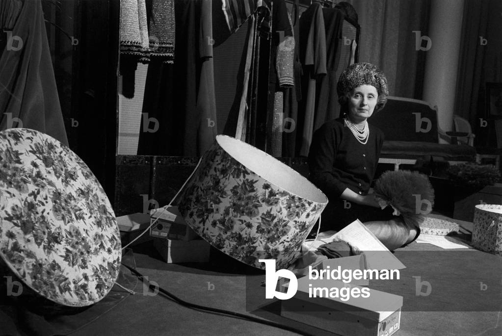 Biki sitting on the ground in her workshop among clothes and boxes