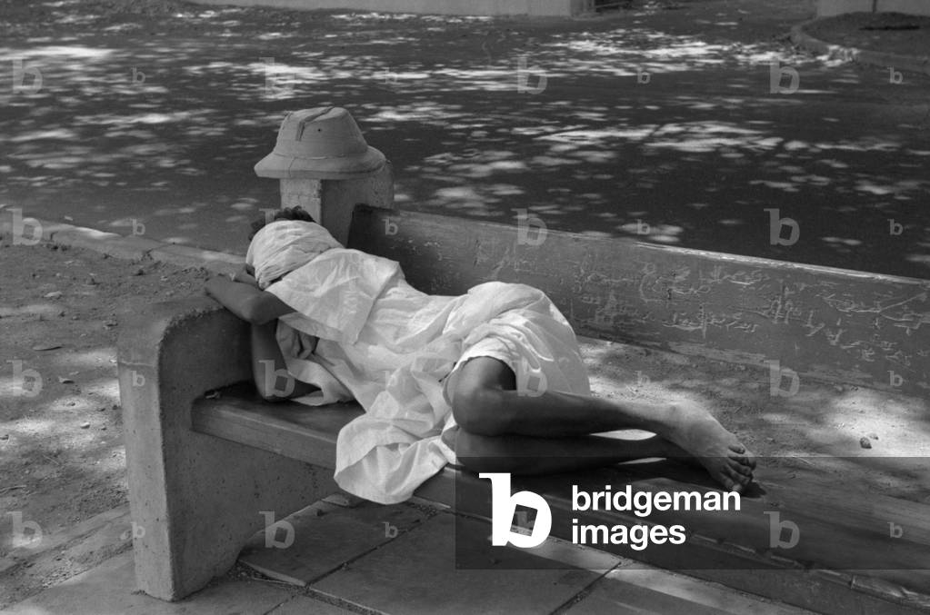 Sudanese man lying on a bench and sleeping, Khartoum, April 1965 (b/w photo)