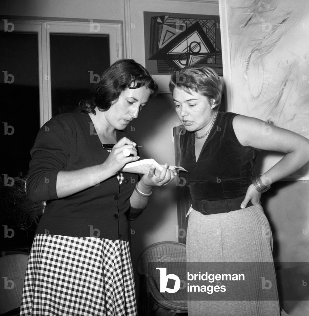 Fernanda Pivano beside a woman writing something on a book , Milan, Italy
