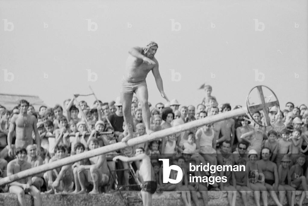 15th August 1969 - Bathers flock on the jetty to see the balancing game on the pole, Italy, 1969 (b/w photo)