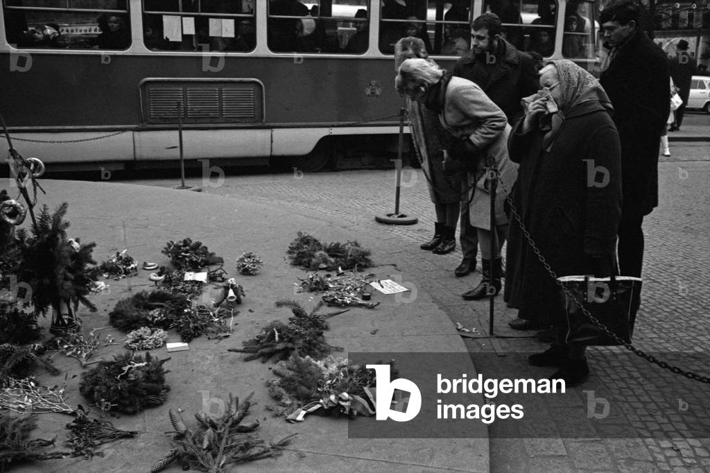 Some people looking at some memorial garlands at the foot of the equestrian statue of Saint Wenceslas on Wenceslas Square, Prague, Czech Republic, December 1968 (b/w photo)