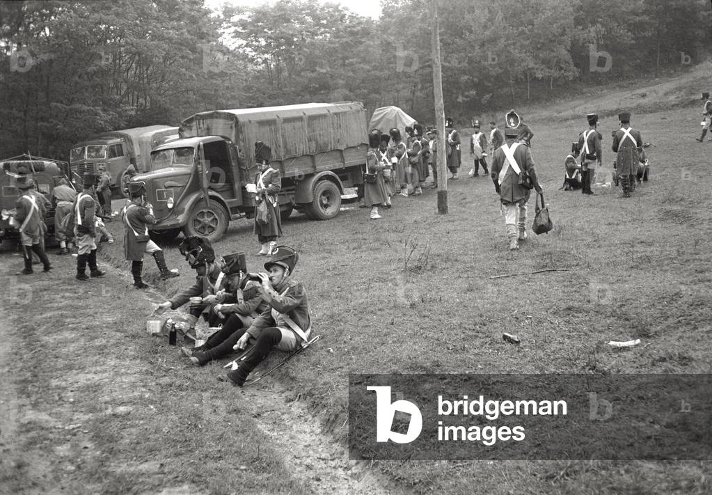 Extras wearing stage costumes have something to eat on the grass, during filming of King Vidor's 'War and Peace', 1955 (b/w photo)