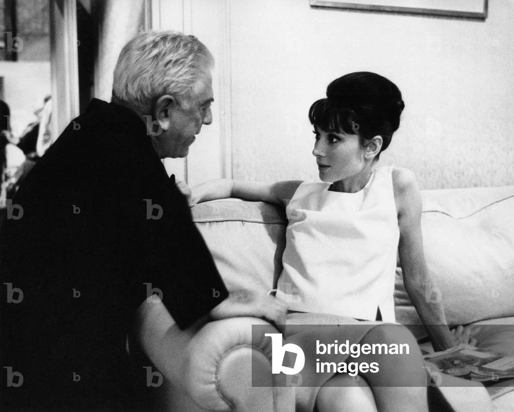Audrey Hepburn talks to a man, sitting on a sofa, 1965 (b/w photo)