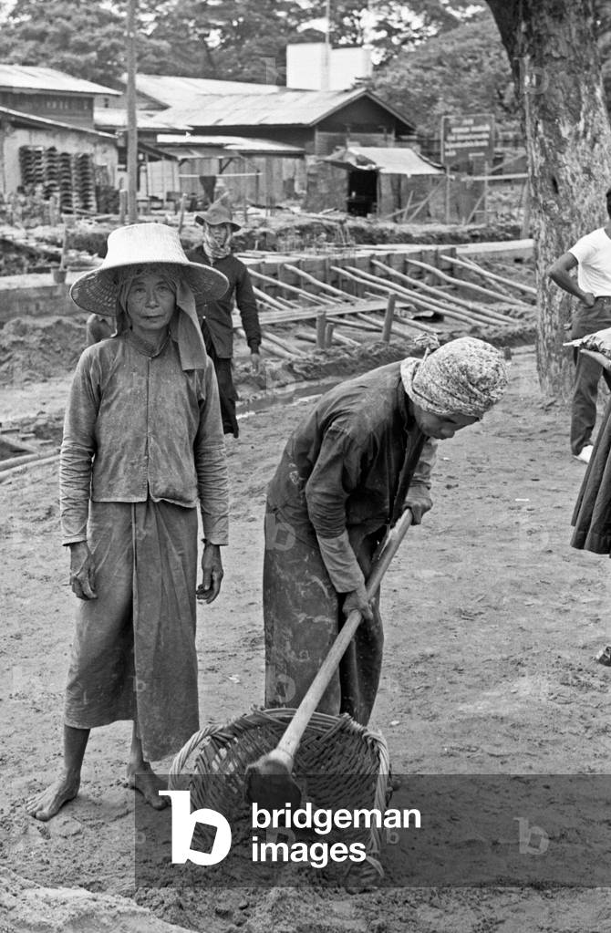 Thai woman hoeing the ground in a building site, Bangkok, 1961 (b/w photo)