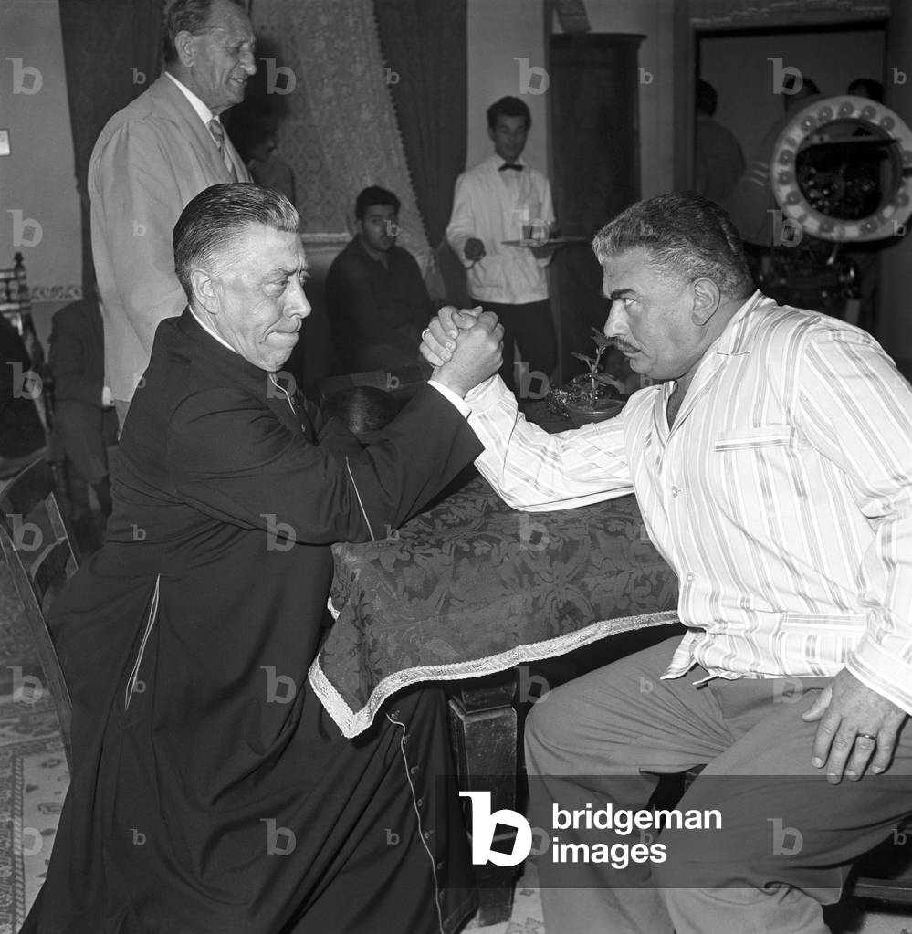 Italian actors Fernandel and Gino Cervi arm wrestling on the set, Italy, 1961 (b/w photo)