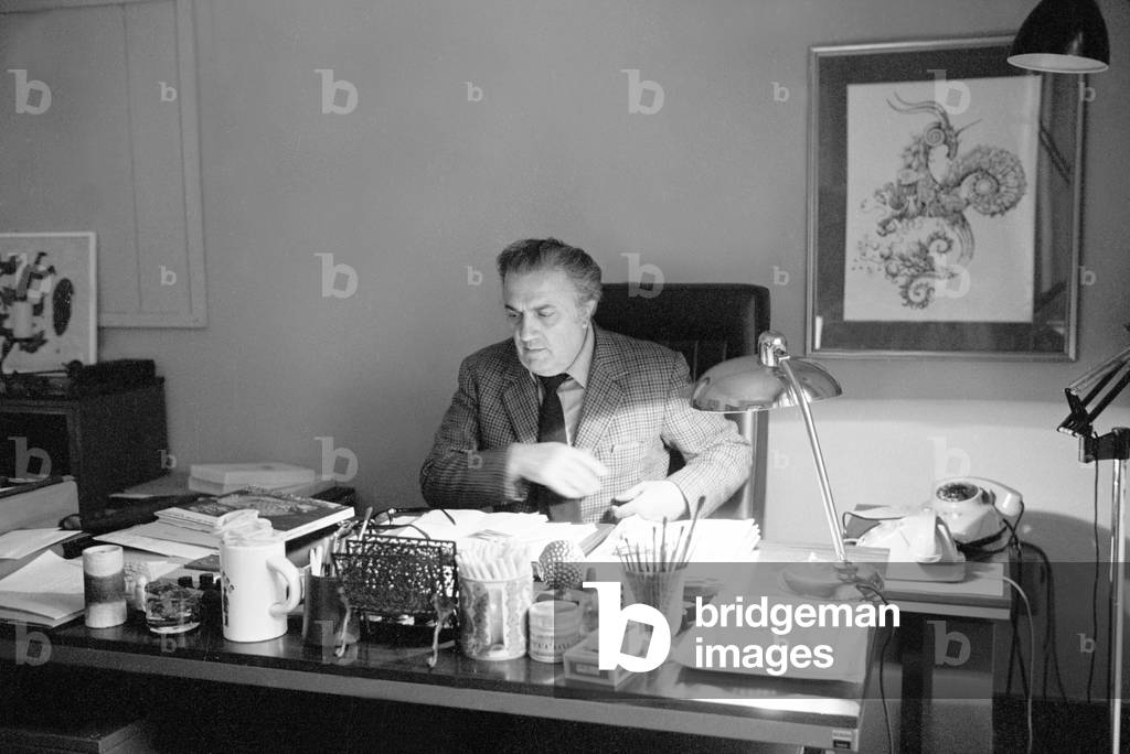Federico Fellini sitting at his desk, Italy, 1960 (b/w photo)