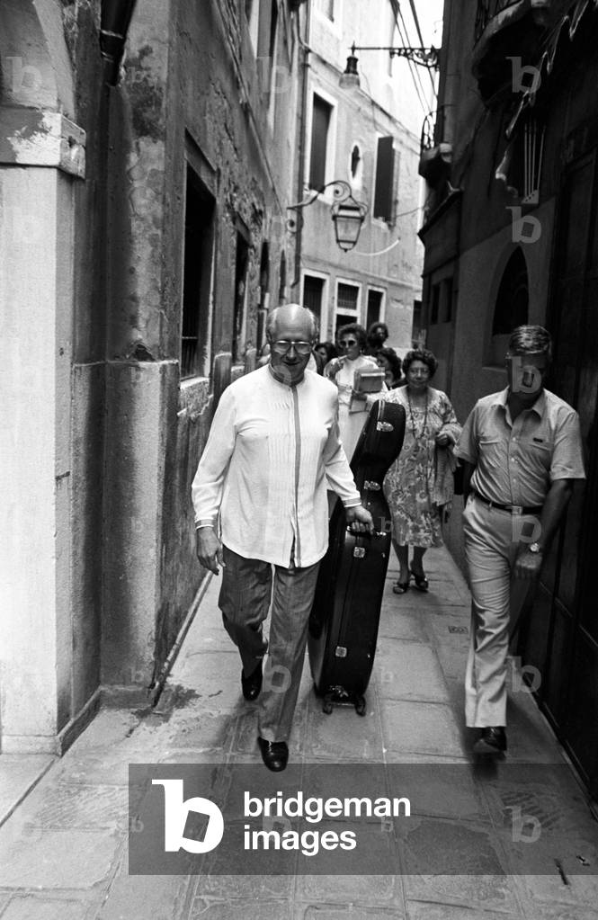 Slava Rostropovich walking in a narrow street with his cello
