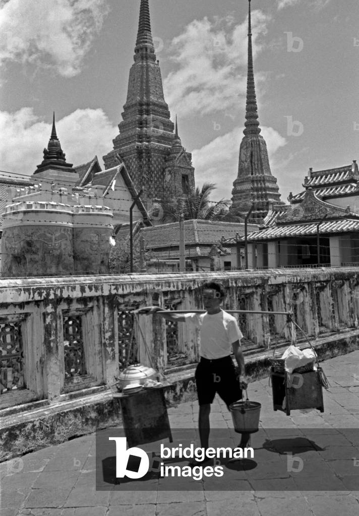Thai man carrying some items on a makeshift scale resting on his shoulder, Bangkok, 1961 (b/w photo)