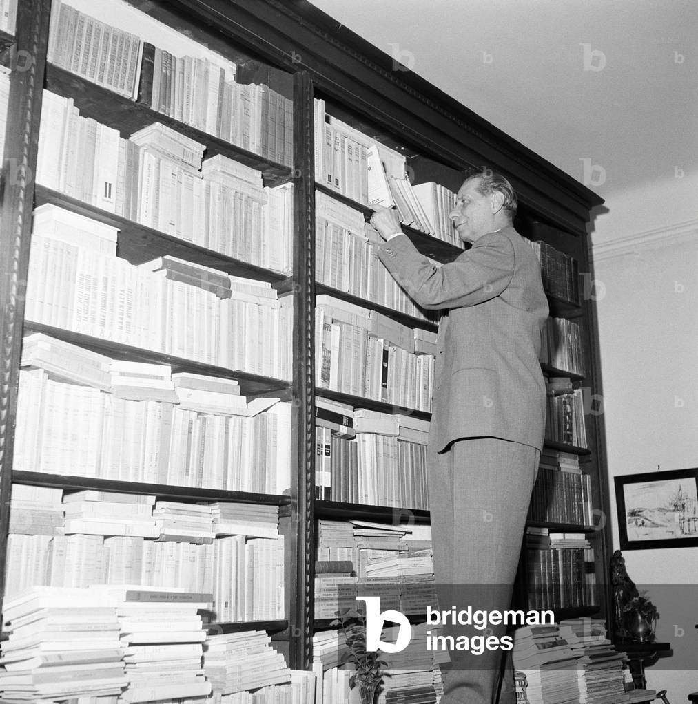Giuseppe Ravegnani draws a book out from a library case, Italy