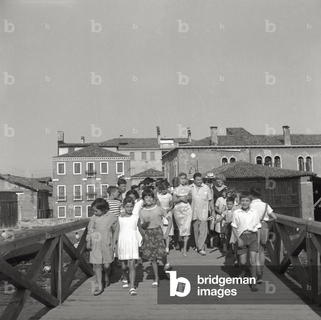 Abbe Lane and Xavier Cugat on a Venetian bridge with crowds of kids, 1956 (b/w photo)
