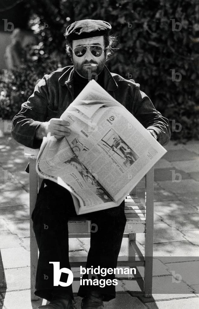 Lucio Dalla seated outside and holding a newspaper in his hands