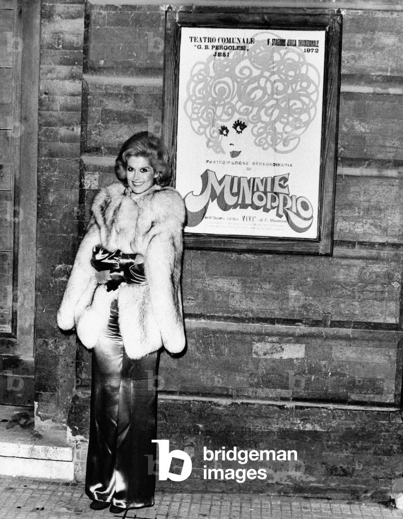 Minnie Minoprio smiling beside a poster portraying her