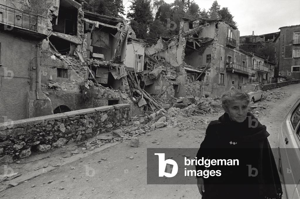 An old woman is walking along the debris, 1980 (b/w photo)