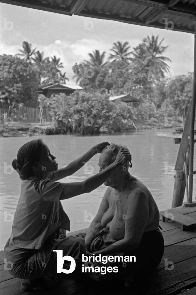 A woman combing an old woman sitting into a palafitte along the Chao Phraya River, Bangkok, 1961 (b/w photo)