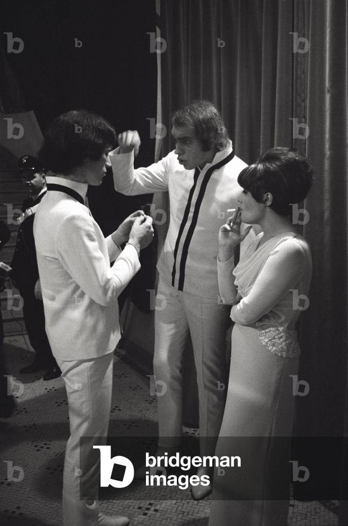 Two men are chatting while a woman is smoking behind the scenes of the Sanremo Song Festival