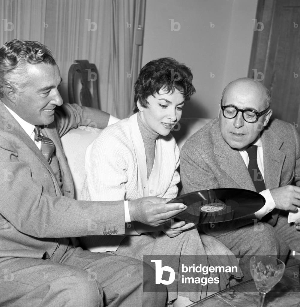 Vittorio De Sica, Gina Lollobrigida and Cesare Zavattini looking at a vynil, Italy, 1956 (b/w photo)
