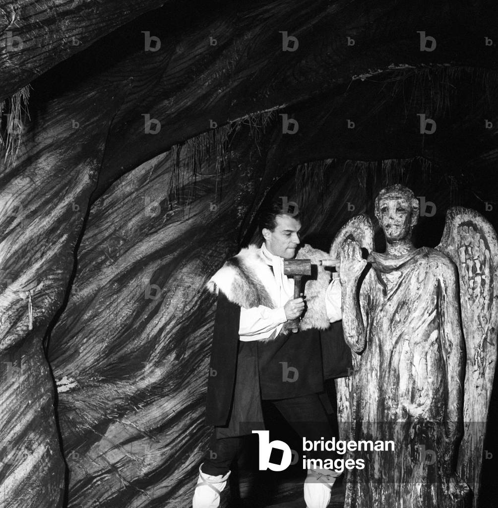 Giorgio Albertazzi with a hammer and a chisel in his hands, next to a statue, 1957 (b/w photo)