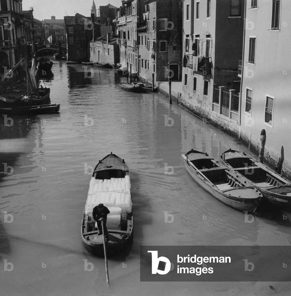 A boat carrying ice in a canal, Chioggia, Italy, March 1954 (b/w photo)
