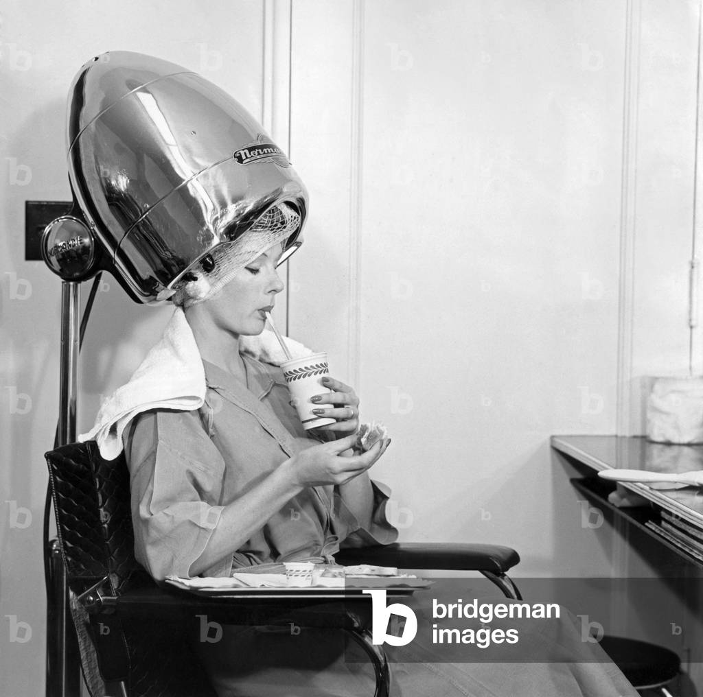 A woman drinking something under a hair drier
