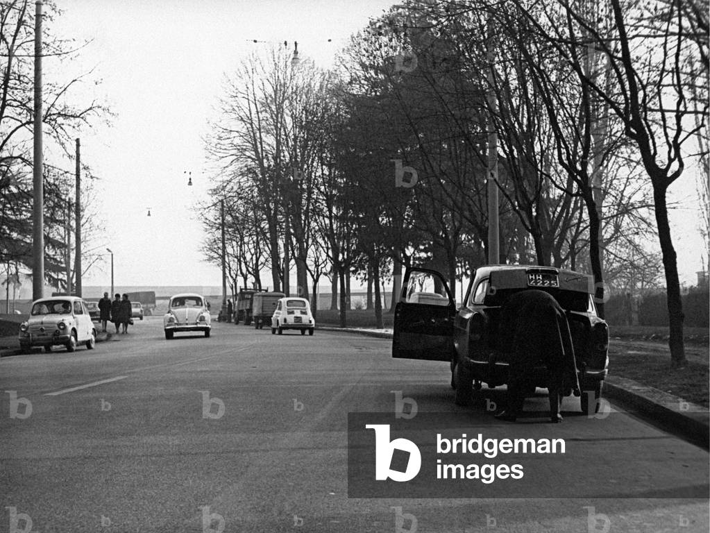 A car with open door is stopped on the edge of the street , Italy
