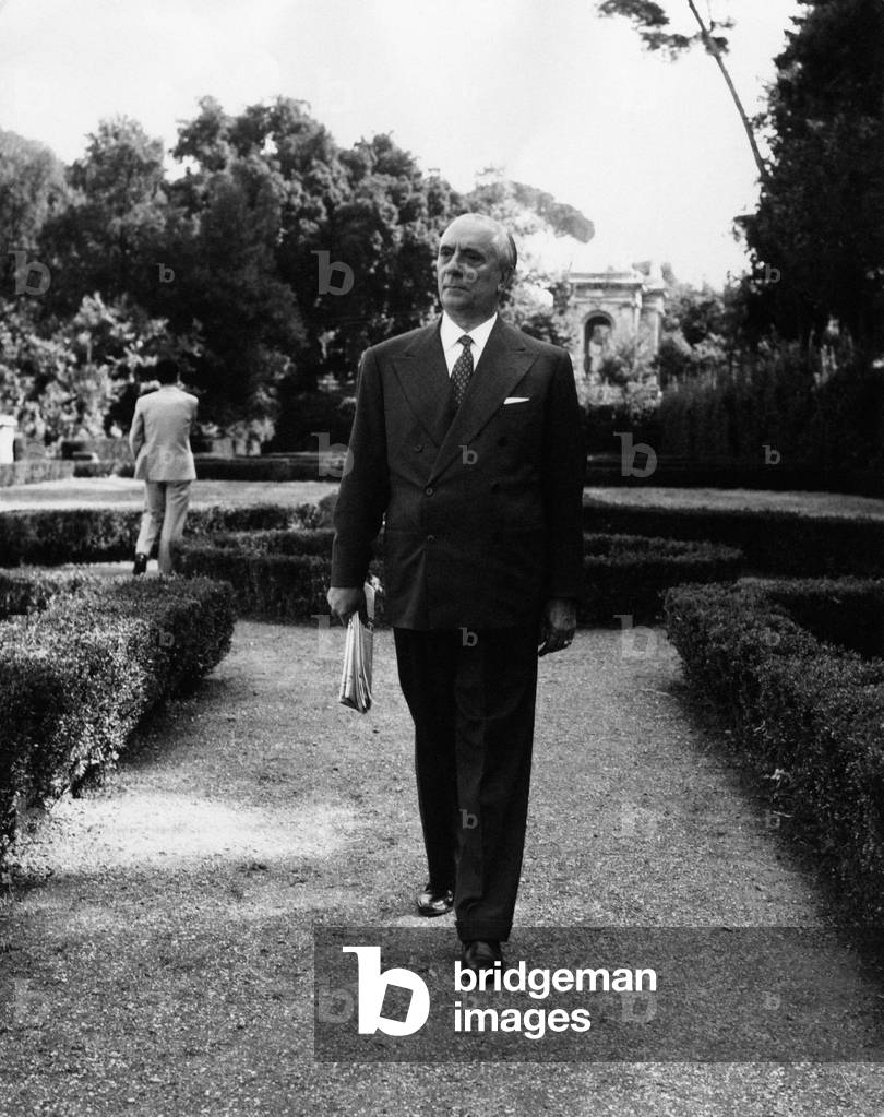 Pietro Campilli standing in a park with a serious looking, holding a newspaper in his hand