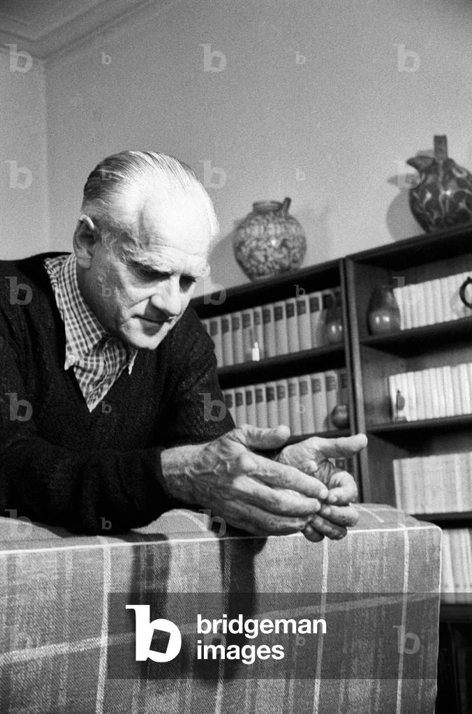 Alberto Moravia leaning on the back of a sofa