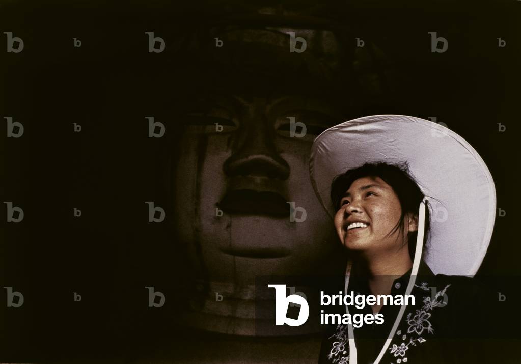 A female tourist in a temple inside Mogao caves, in front of a giant statue of Buddha, 1982 (photo)