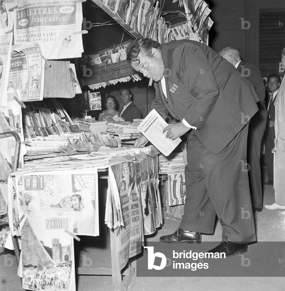 Orson Welles buying some newspapers, Rome, Italy, 1958 (b/w photo)