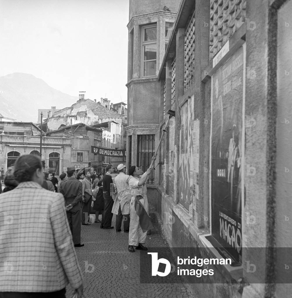 A bill sticker sticking up electoral posters during the regional election in Trentino-Alto Adige/Sudtirol, Italy, November 1952 (b/w photo)