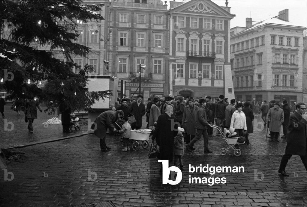 Some people walking on Old Town Square beside a Christmas Tree from the Bohemian forests, Prague, Czech Republic, December 1968 (b/w photo)