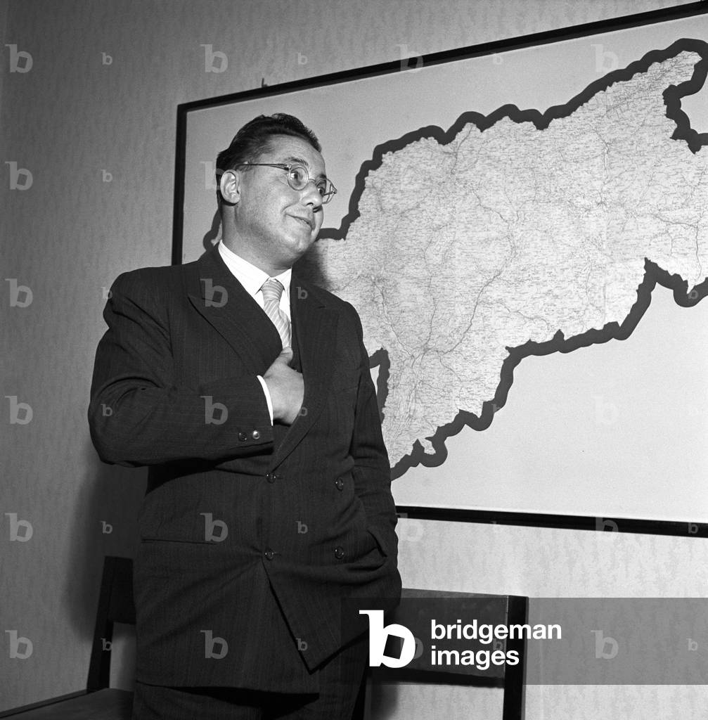 Italian lawyer and politician Tullio Odorizzi of Christian Democratic Party, president of Trentino-Alto Adige/Sùdtirol, smiling near a map of South Tyrol during the regional election, Italy, November 1952 (b/w photo)