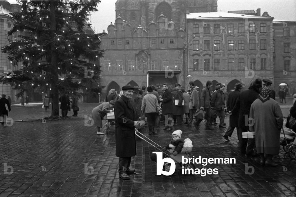 Some people walking on Old Town Square beside a Christmas Tree from the Bohemian forests, Prague, Czech Republic, December 1968 (b/w photo)