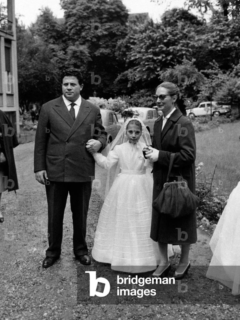 Sarah Ferrati and Luigi Infantino holding by the hand Monica Infantino at her holy communion