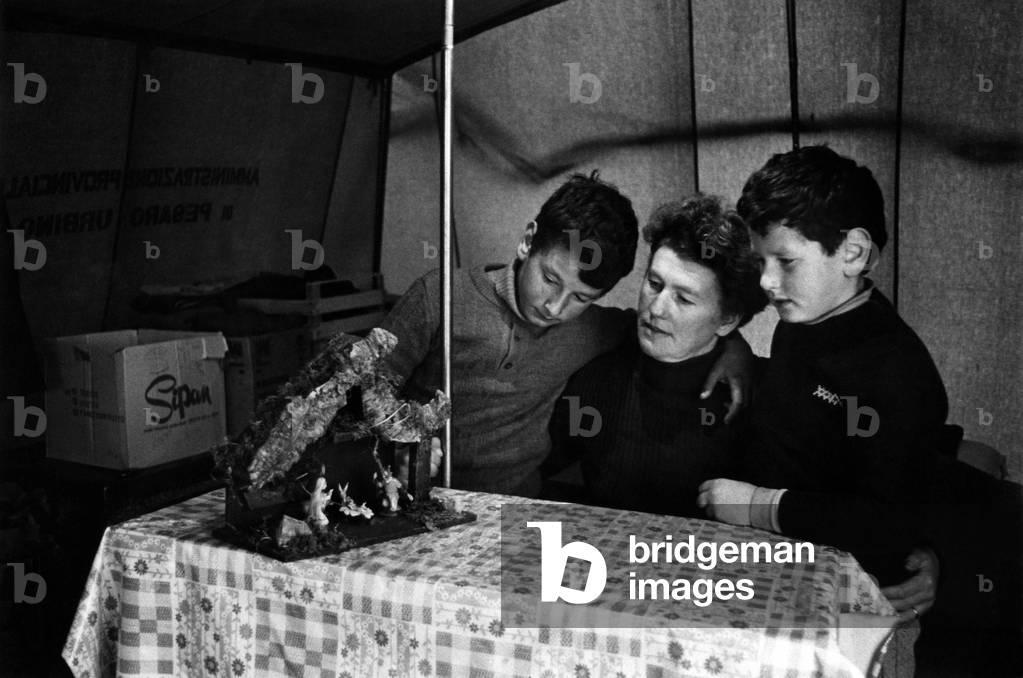 A woman embraced with her children in front of a traditional Christmas nativity scene